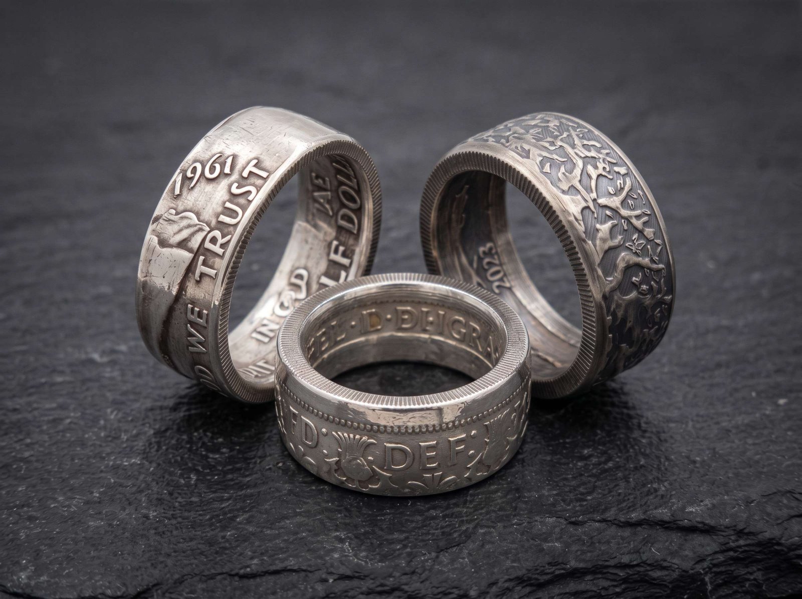 Three finished coin rings on dark slate
